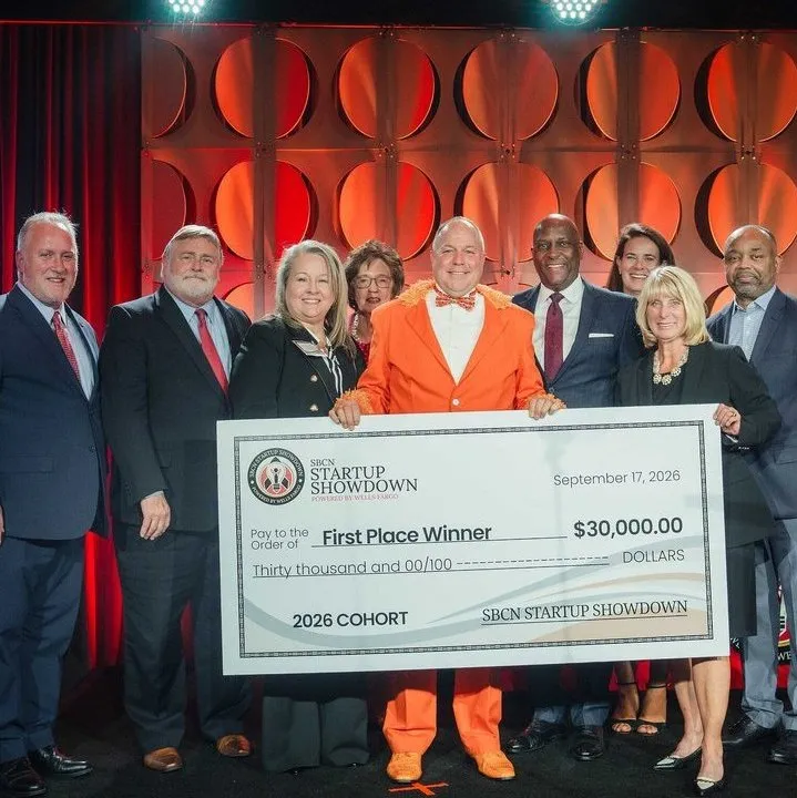 Eight officials stand with a winner holding a $30,000 Startup Showdown check onstage.